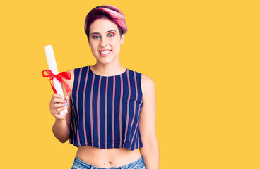 Young beautiful woman with pink hair holding graduate degree diploma looking positive and happy standing and smiling with a confident smile showing teeth