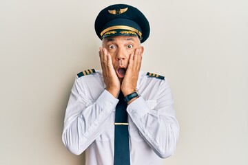 Handsome middle age mature man wearing airplane pilot uniform afraid and shocked, surprise and...