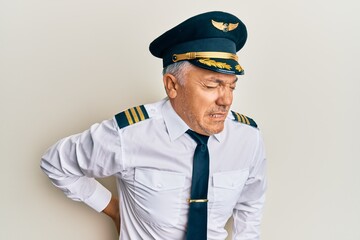 Handsome middle age mature man wearing airplane pilot uniform suffering of backache, touching back with hand, muscular pain