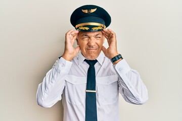 Handsome middle age mature man wearing airplane pilot uniform with hand on head, headache because...