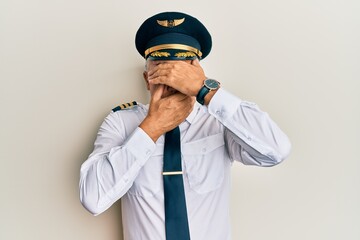 Handsome middle age mature man wearing airplane pilot uniform covering eyes and mouth with hands,...