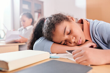Exhausted or bored schoolgirl in casualwear keeping head on desk while napping
