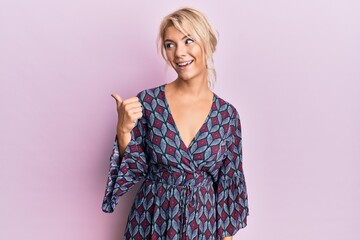 Obraz premium Young blonde girl wearing casual clothes smiling with happy face looking and pointing to the side with thumb up.