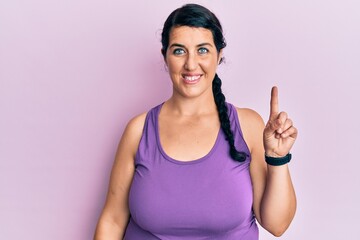Plus size brunette woman wearing sportswear smiling with an idea or question pointing finger up with happy face, number one