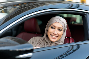 Smiling muslim woman test driving car in urban city