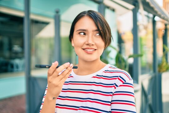 Young latin girl smiling happy sending voice message using smartphone at the city