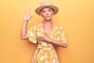 Beautiful blonde woman on vacation wearing summer hat and dress over yellow background Swearing...