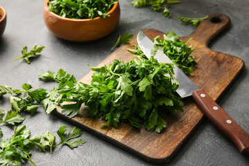 Cutting board with fresh parsley and knife on grey background