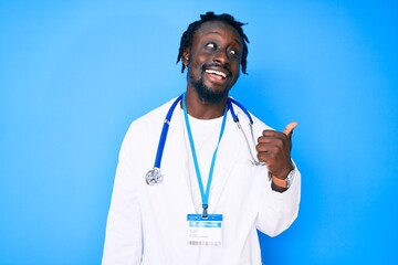 Young african american man with braids wearing doctor stethoscope and id pass smiling with happy face looking and pointing to the side with thumb up.