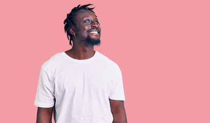 Young african american man with braids wearing casual white tshirt looking away to side with smile on face, natural expression. laughing confident.