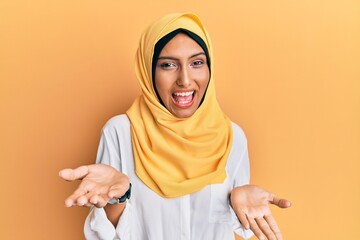 Young brunette arab woman wearing traditional islamic hijab scarf smiling cheerful with open arms as friendly welcome, positive and confident greetings