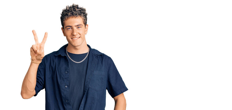 Young handsome man wearing casual clothes smiling with happy face winking at the camera doing victory sign. number two.