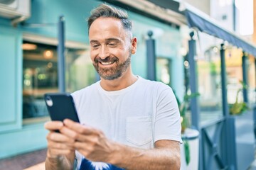 Middle age handsome man smiling happy using smartphone at the city.