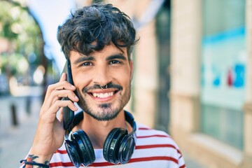 Young hispanic man wearing headphones and talking on the smartphone at street of city