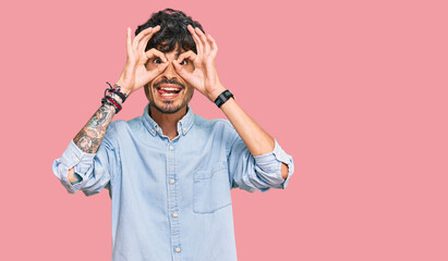 Young hispanic man wearing casual clothes doing ok gesture like binoculars sticking tongue out, eyes looking through fingers. crazy expression.