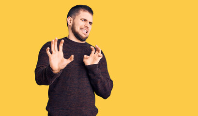 Young handsome man wearing casual sweater disgusted expression, displeased and fearful doing disgust face because aversion reaction. with hands raised