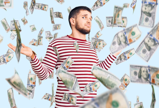 Young handsome man wearing striped sweater clueless and confused expression with arms and hands raised. doubt concept.