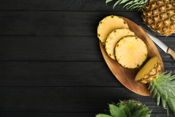 Whole and cut pineapples on black wooden table, flat lay. Space for text