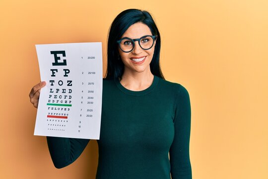 Young caucasian woman holding optometry glasses and eyesight test looking positive and happy standing and smiling with a confident smile showing teeth