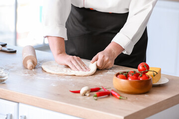 Mature female chef with dough for tasty pizza in kitchen