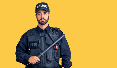 Young hispanic man wearing police uniform holding baton thinking attitude and sober expression looking self confident