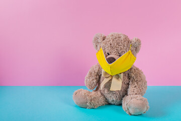 Toy Teddy bear wearing yellow mask on its face and sitting on colorful floor. Copy space. Concept...