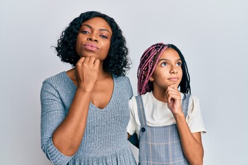 Beautiful african american mother and daughter wearing casual clothes and hugging with hand on chin thinking about question, pensive expression. smiling with thoughtful face. doubt concept.