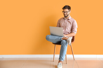Man with laptop studying online near color wall