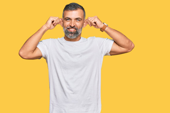 Middle age handsome man wearing casual white tshirt smiling pulling ears with fingers, funny gesture. audition problem