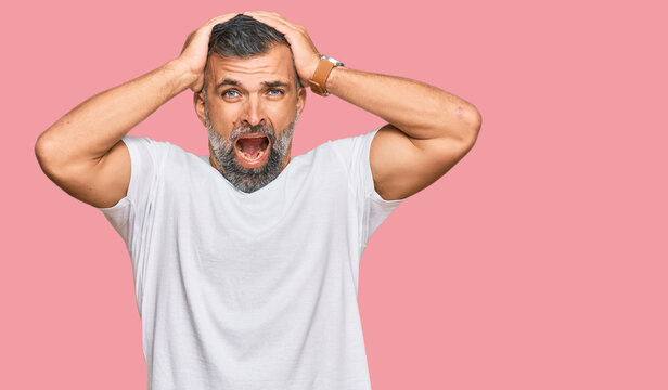 Middle age handsome man wearing casual white tshirt crazy and scared with hands on head, afraid and surprised of shock with open mouth