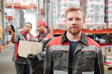 Successful young bearded man in workwear looking at you against colleagues