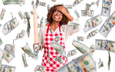 Young african american woman wearing apron holding rolling pin stressed and frustrated with hand on head, surprised and angry face