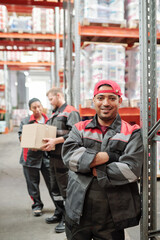 Happy young Latino worker in grey uniform and gloves crossing arms by chest