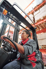 Naklejka premium Young mixed-race female in workwear sitting by steer inside industrial machine