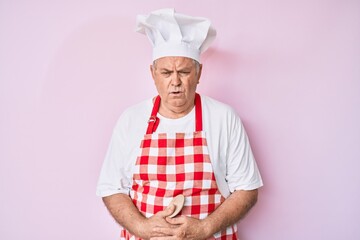 Senior grey-haired man wearing professional baker apron with hand on stomach because indigestion, painful illness feeling unwell. ache concept.