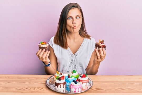 Young caucasian woman holding cake slices making fish face with mouth and squinting eyes, crazy and comical.