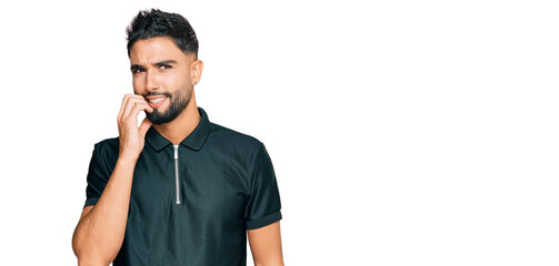 Young man with beard wearing sportswear looking stressed and nervous with hands on mouth biting nails. anxiety problem.
