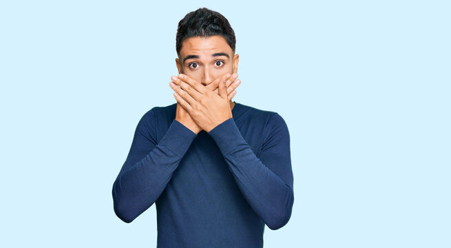 Young man with beard wearing casual blue winter sweater shocked covering mouth with hands for mistake. secret concept.