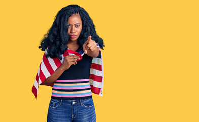 Beautiful african american woman holding united states flag pointing with finger to the camera and to you, confident gesture looking serious