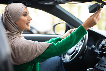Young muslim woman driving alone adjusting rearview mirror