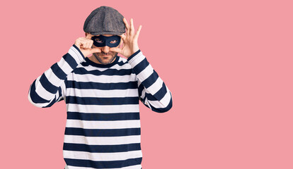 Young handsome man wearing burglar mask trying to open eyes with fingers, sleepy and tired for...