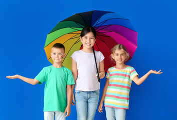 Little children with rainbow umbrella on color background