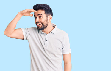 Fototapeta premium Young handsome man with beard wearing casual polo very happy and smiling looking far away with hand over head. searching concept.
