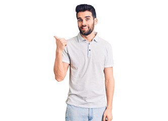 Young handsome man with beard wearing casual polo smiling with happy face looking and pointing to the side with thumb up.