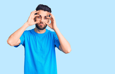 Naklejka premium Young handsome man with beard wearing casual t-shirt trying to open eyes with fingers, sleepy and tired for morning fatigue