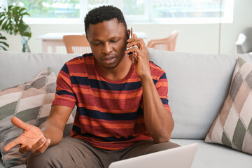 Stressed African-American man talking by phone at home