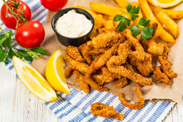 Crispy Breaded Clam Strips Snack Size. Deep Fried Breaded Clams Fingers and French Fried Potatoes with Tartar Dipping Sauce on a wooden board. Selective focus.