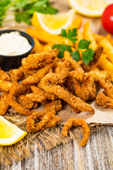 Crispy Breaded Clam Strips Snack Size. Deep Fried Breaded Clams Fingers and French Fried Potatoes with Tartar Dipping Sauce on a wooden board. Selective focus.