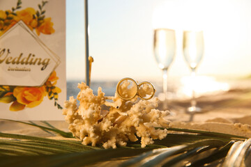 Coral with gold rings and wedding invitation on sandy beach