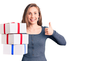 Young beautiful blonde woman holding birthday gift smiling happy and positive, thumb up doing excellent and approval sign